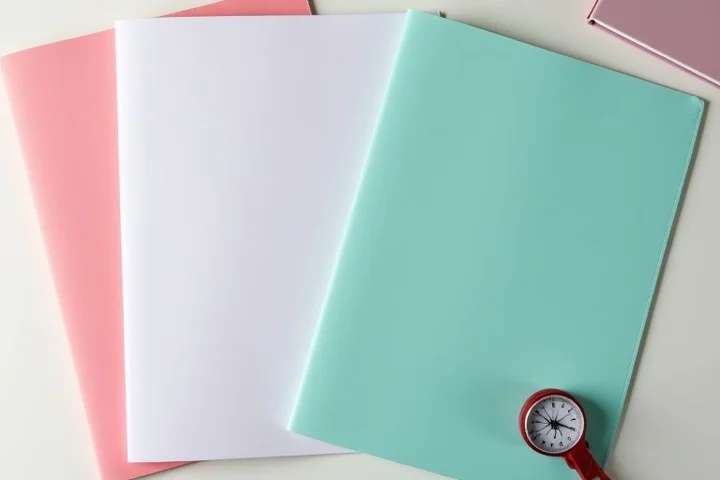 Three plain color-coded folders rest on a clean tabletop beside a compass and a folded notebook